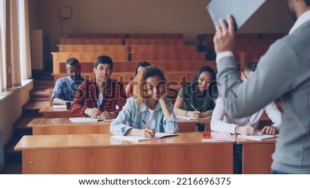 Group of students is listening to teacher and writing sitting at tables in classroom while male professor is talking and gesturing. Higher education and people concept. ストックフォト © 