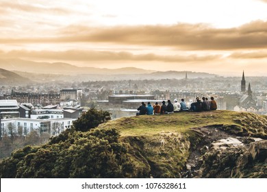 Group of students overlook Edinburgh at sunset from Arthur's Seat. with orange tones - Shutterstock ID 1076328611