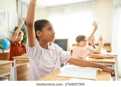 Group of students raising hands eagerly in classroom, representing active participation and engaging learning environment