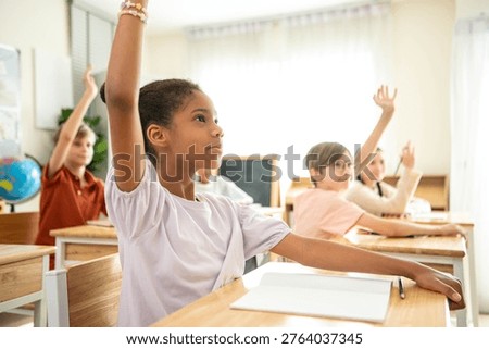 Group of students raising hands eagerly in classroom, representing active participation and engaging learning environment