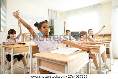 Group of students raising hands eagerly in classroom, representing active participation and engaging learning environment