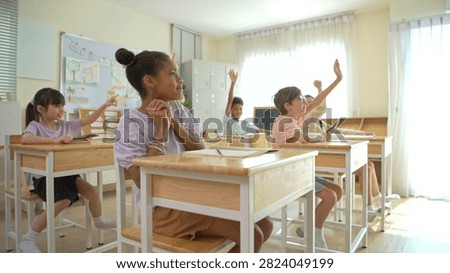 Group of students raising hands eagerly in classroom, representing active participation and engaging learning environment