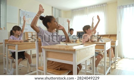 Group of students raising hands eagerly in classroom, representing active participation and engaging learning environment
