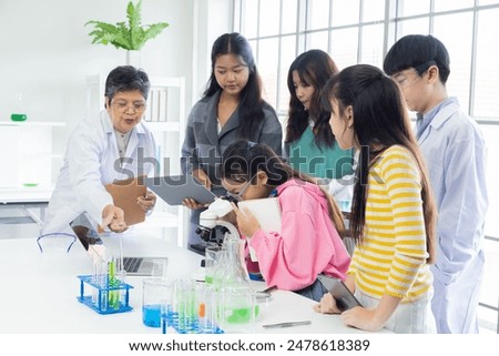 Group of students in science class using laptops and microscopes, conducting experiments. Young diverse pupils focused on research and senior teacher supervision. educations and back to school concept