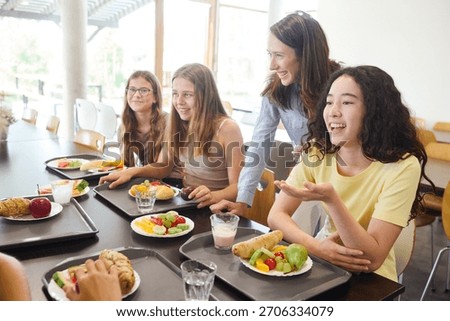 A group of students shares a laugh while enjoying fresh and nutritious meals in a well-organized school cafeteria, fostering camaraderie and joy. A teacher engages warmly, highlighting the positivity.