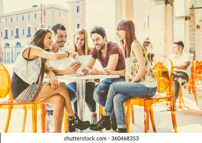 Group of students sitting in a cafe bar looking at tablet - Young cheerful friends having fun with portable computer - Active people watching a funny streaming movie online - Powered by Shutterstock