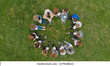 A Group Of Students Are Sitting In A Circle And Books On The Grass.