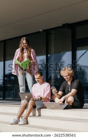 Group of students studying and using laptops outside a modern university building on a sunny day