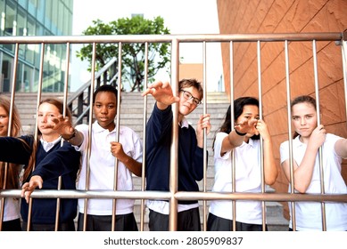 Group of students in uniforms posing playfully behind a metal fence.