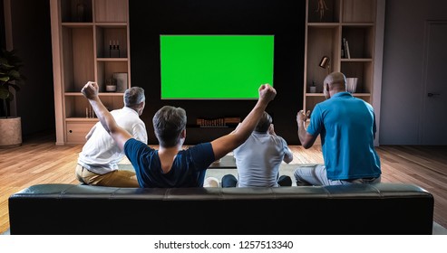 A group of students is watching a TV and celebrating some joyful sports moment, sitting on the couch in the living room. The living room is made in 3D. TV is green screen for further editing. - Powered by Shutterstock