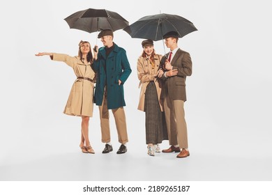 Group Of Stylish Young People In Coats And Jackets Posing With Umbrella Isolated Over White Background. Autumn, Fall Fashion Collection. Concept Of Retro Fashion, Style, Youth Culture, Beauty, Ad