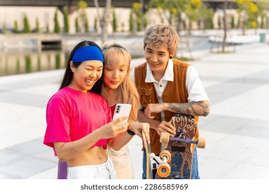 Group of Stylish youth people Asian man and woman friends have fun urban outdoor lifestyle using mobile phone with internet during skating on longboard skate in the city together on summer vacation. - Powered by Shutterstock