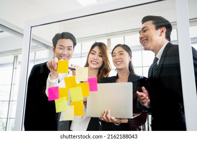 Group of successful Asian businessmen and women teamwork. Brainstorm meeting with sticky paper notes on the glass wall for new ideas. Using agile methodology for business in a tech start-up office. - Powered by Shutterstock