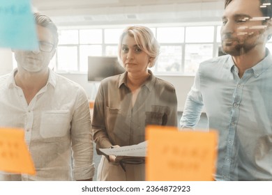 Group of successful businesspeople using sticky notes, agile methodology for productivity working together in modern office. Colleagues planning startup, communication at workplace. Teamwork, scrum - Shutterstock ID 2364872923