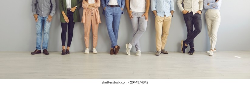 Group of successful confident business people in smart and casual wear standing in studio. Team of employees leaning on grey office wall. Cropped shot of people's legs in classic pants and jeans - Shutterstock ID 2044374842