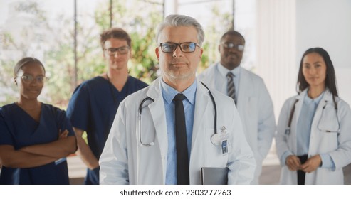 Group of Successful Multiethnic Team of Female and Male Doctors, Nurses and Healthcare Professionals Posing for Camera and Smiling. Portrait of a Confident Middle Aged Physician Standing First in Line