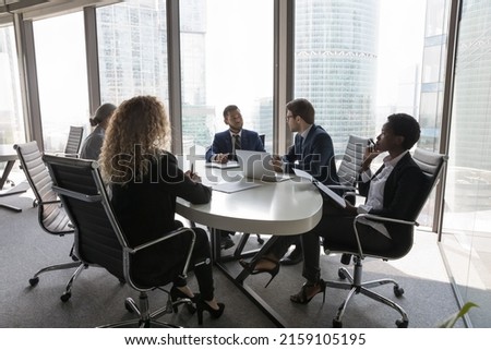 Group of successful young multi ethnic businesspeople partners gathered in modern office boardroom to solve common business, work on collaborative project, strategizing together. Negotiation concept