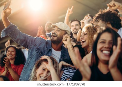 Group Of Supporters Watching Football Game And Making Self-portrait With Smartphone At Stadium. Multi-ethnic People Enjoying Watching A Game At Stadium And Taking A Selfie.