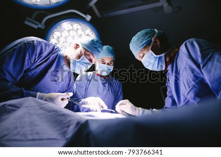 Group of surgeons doing surgery in hospital operating theater. Medical team doing critical operation.