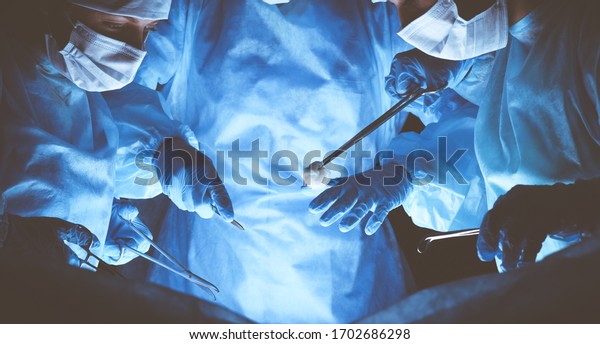 Group of surgeons wearing safety masks performing\
operation. Medicine\
concept