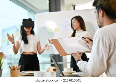 A group of tech developers brainstorming about their new virtual innovation project, testing a VR glasses, a man sketching scales and noting a mistakes from their innovation.