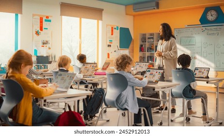 Group of Tech-Savvy Primary School Children Working on Their Laptop and Tablet Computers in Class. Young Female Teacher Educating Kids on Internet Safety, Basic Programming Languages and Formulas - Powered by Shutterstock
