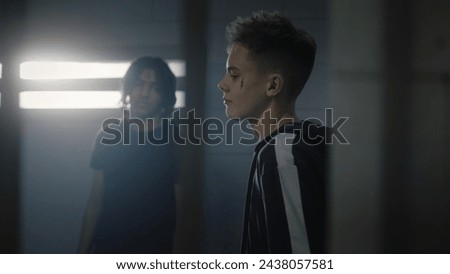 Group of teen prisoners talk with each other in jail cell. Diverse teenagers serve imprisonment term for crime in detention center. Young inmates in prison. Justice system. View through metal bars.