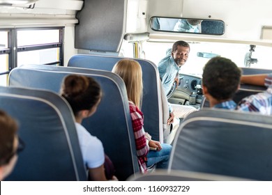 Group Of Teen Scholars Riding School Bus And Talking With Happy Mature Driver