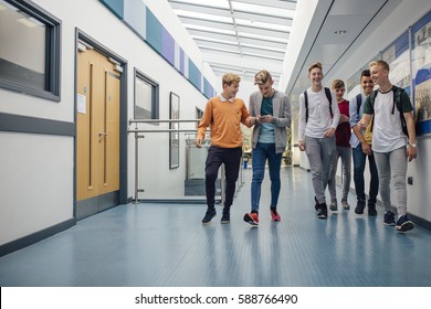 Group Of Teenage Boys Are Walking Down The School Hall Together To Go For Their Lunch Break. They Are Talking And Laughing And Some Of The Boys Are Using Smart Phones.