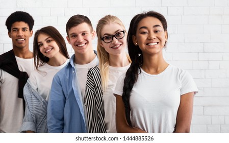 Group of teenage friends standing in line and looking at camera, white brick wall
