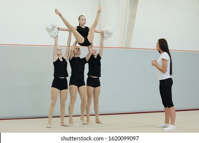 Group Of Teenage Girls Holding Arms And Hip Of Dancer With Pompoms While Performing Cheerleading Stunt While Trainer Giving Advices