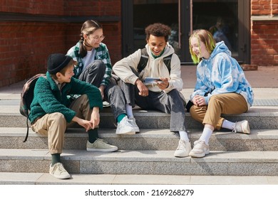 Group of teenage students sitting outside school buildings and watching funny video on smartphone - Powered by Shutterstock