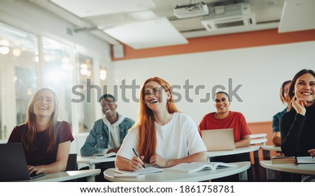 Group of teenage students smiling during the lecture in classroom. University students laughing in classroom.