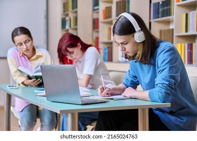 Group of teenage students study sitting at desk in library, in focus is guy using laptop - Powered by Shutterstock