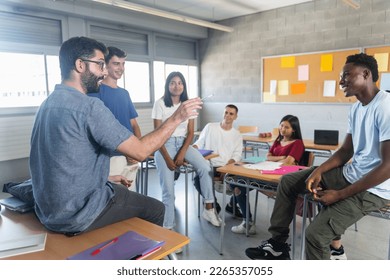 Group of teenager students with young teacher at classroom, sitting talking and sharing conversation together - Powered by Shutterstock