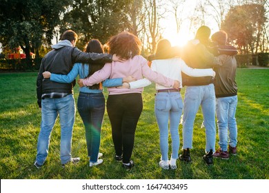 Group Of Teenagers Of Different Cultures Hugging Each Other At The Park At Sunset - Teamwork Of Young People Arranged From Behind - Six Men And Women Having Fun Together