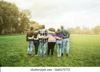 Group Of Teenagers Of Different Cultures Hugging Each Other At The Park At Sunset - Teamwork Of Young People Arranged From Behind - Six Men And Women Having Fun Together