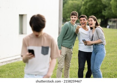 Group Of Teenagers Laughing And Pointing At Boy. Cyber Bullying Concept