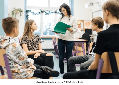 Group Of Teenagers Sitting In A Circle In Front Of Them Facing The Nurse With A Green Notebook