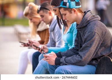 Group of teenagers sitting outdoors using their mobile phones - Shutterstock ID 267444602