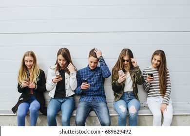 Group Of Teenagers Sitting Outdoors Using Their Mobile Phones