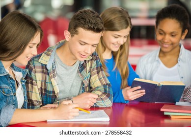 A group of teenagers sitting at the table in cafe and doing homework.