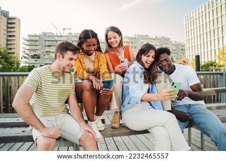 Group of teenagers smiling while watching and enjoying some funny videos next to the university. International young students looking and searching different websites joking together as a leisure