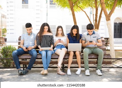 Group Of Teenagers Social Networking Using Several Tech Devices Outdoors