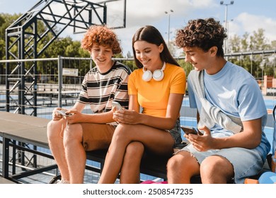 Group of teenagers students high school pupils classmates using different gadgets holding mobile phone play video game browsing internet watching video in sport basketball court sitting outside - Powered by Shutterstock