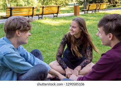 Group Of Teenagers Two Boys And One Girl Sitting In City Park Having Fun And Laughing
