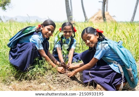 group of teener village school kids planting tree while looking at camera - concept of environmental conservation, volunteers and sustainable lifestyle