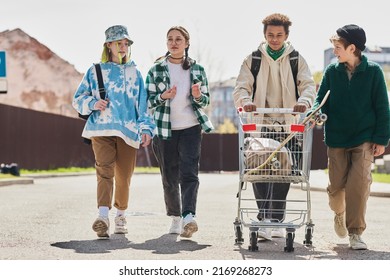 Group Of Teens Walking Along The Street And Carrying Shopping Cart With Their Stuffs