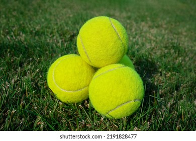 A group of tennis balls stacked in a pyramid on grass. Generic furry fuzzy yellow tennis balls on grass   - Powered by Shutterstock