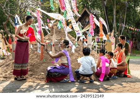Group of Thai women, man and children in colorful traditional Thai costumes decorating sand mountains with flags celebrating Songkran festival in Chiangmai Thailand